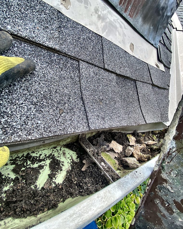 Photo of a roof gutter packed with leaves, sediment and loose rock.